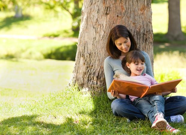 Mãe e filha lendo livro embaixo de árvore (Foto: Shutterstock)